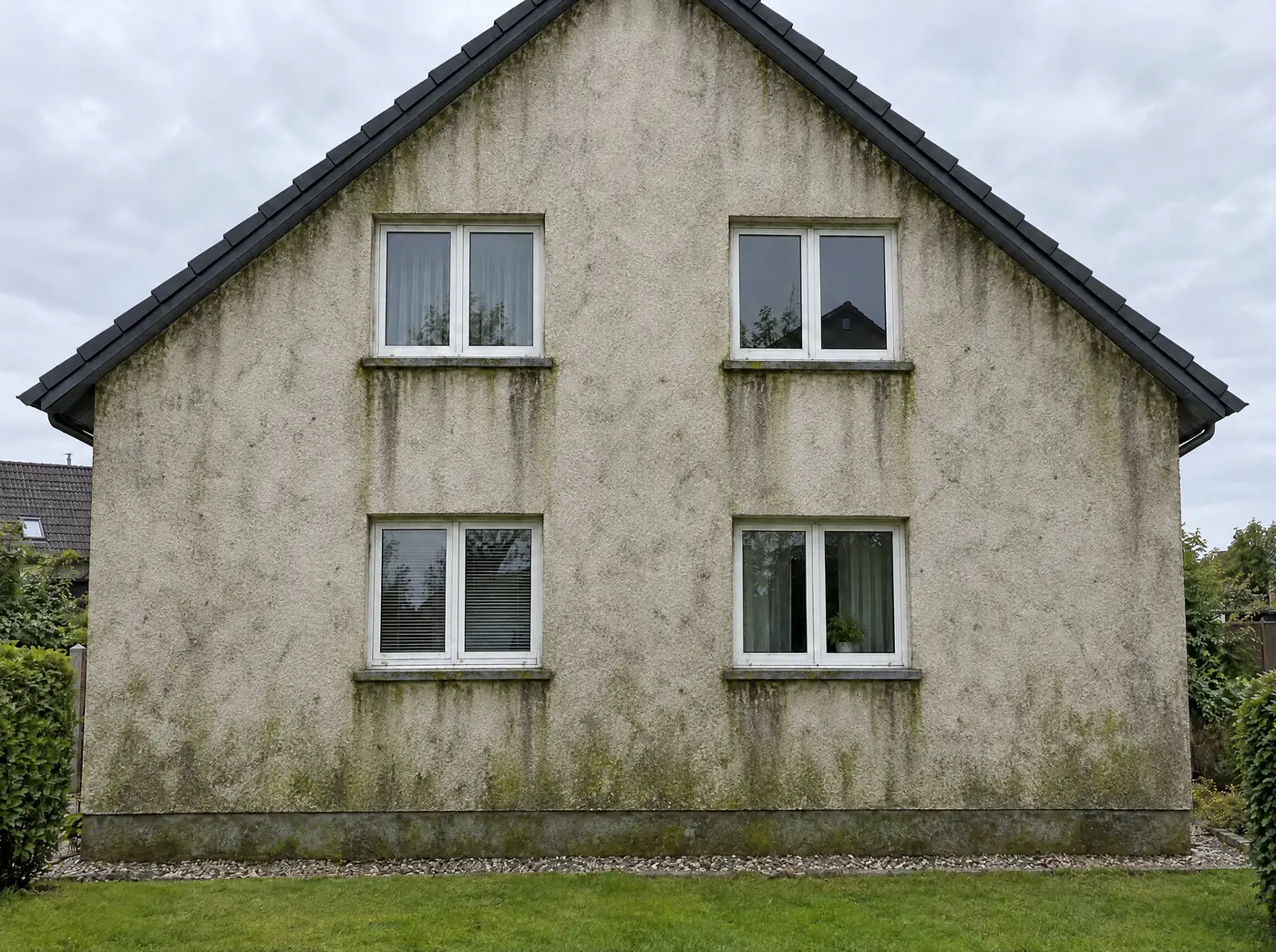 Beispielbild: Hausfassade vor der Reinigung, mit grünen Algen und grauen Schlieren unter den Fenstern