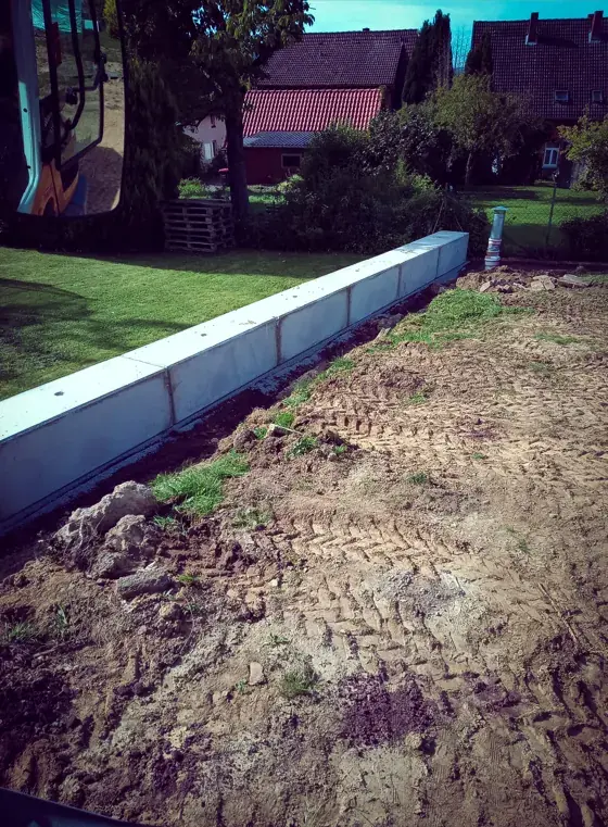 Aufgewühlter Boden entlang einer neuen Mauer aus L-Steinen