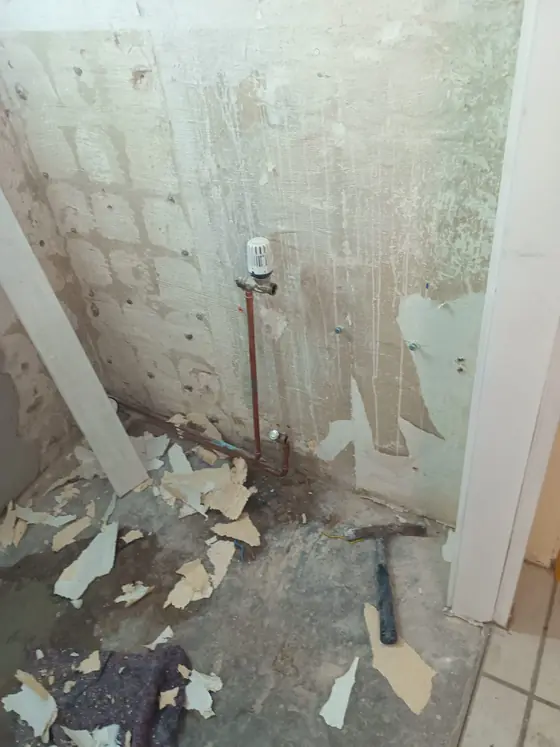 WC vor der Renovierung: Tapete abgerissen, Wand roh, Heizungsrohr frei